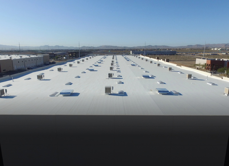 White commercial rooftop with blue skylights and HVAC units against mountain backdrop
