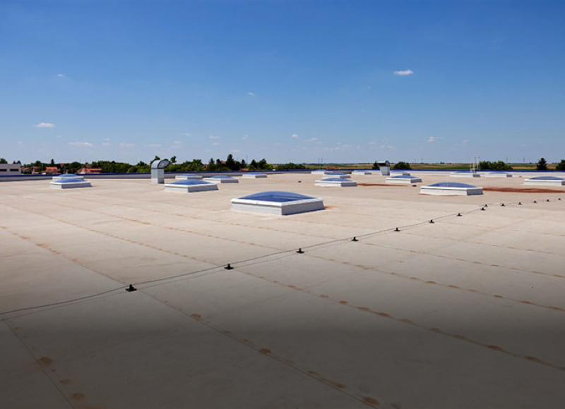 Commercial flat roof with skylights and ventilation units under blue sky