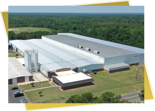 Large industrial manufacturing facility with metal roof surrounded by forest