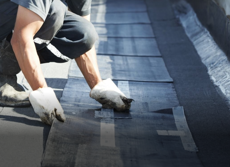 Roofer installing shingles on residential roof with hammer and protective gear