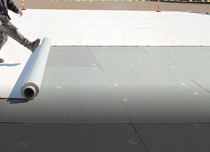 Worker installing gray roofing membrane on flat roof construction site