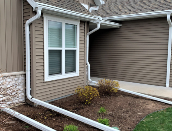 Brown vinyl siding house exterior with white trim and landscaped garden bed