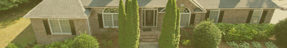 Aerial view of elegant brick house with manicured landscaping and tall trees