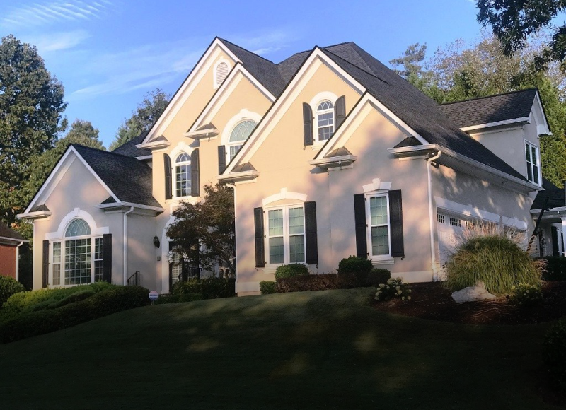 Beautiful two-story suburban home with beige siding, black shutters, and landscaped yard