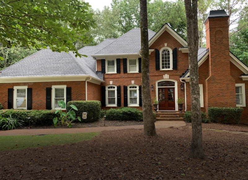 Red brick two-story house with white trim, black shutters and chimney in wooded setting