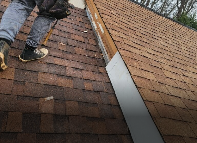 Roofer installing metal flashing on brown asphalt shingle roof valley repair