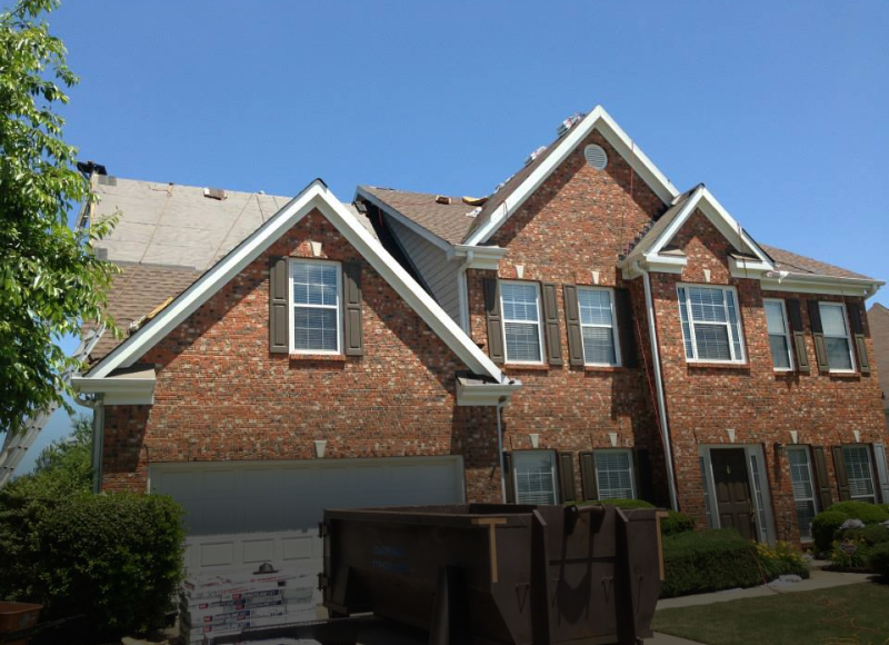 Large two-story brick house with white trim and multiple gabled roofs under blue sky