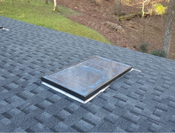 Skylight installed on gray asphalt shingle roof with landscaped yard visible below