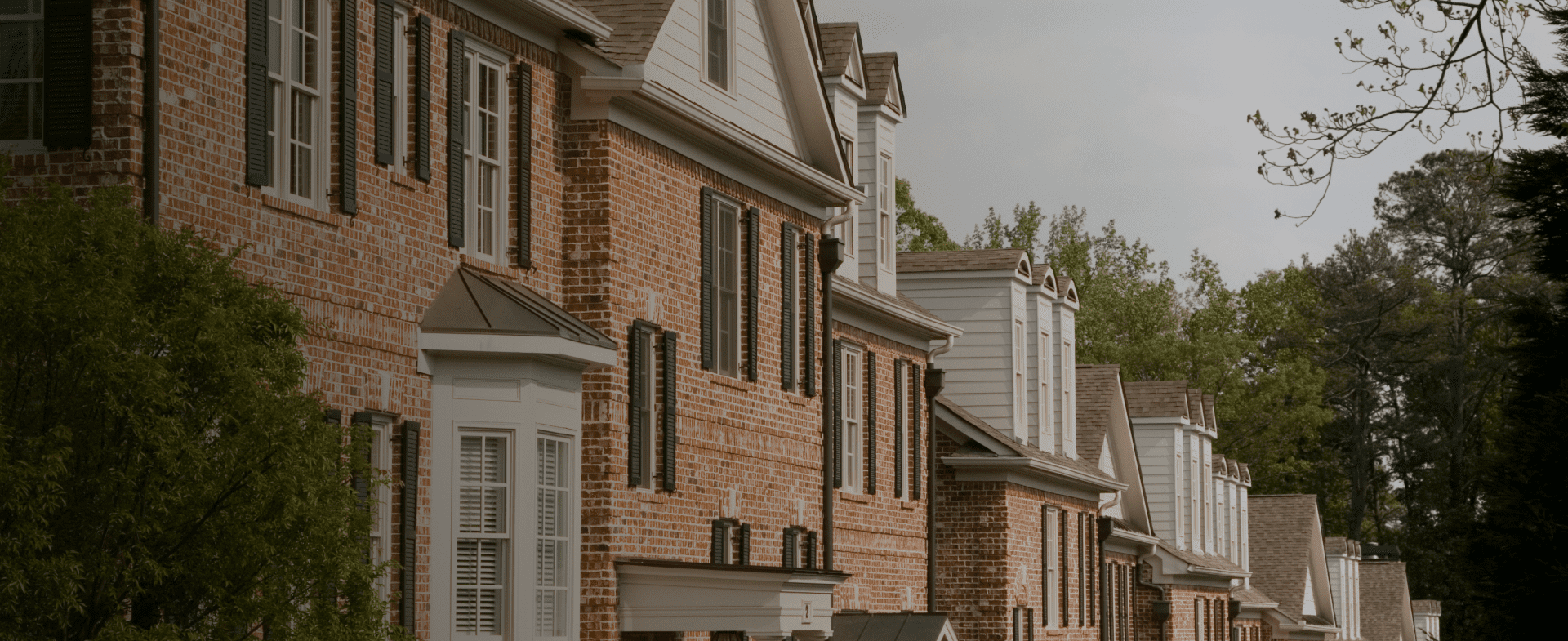 Row of modern brick and white suburban homes with green shutters and landscaping