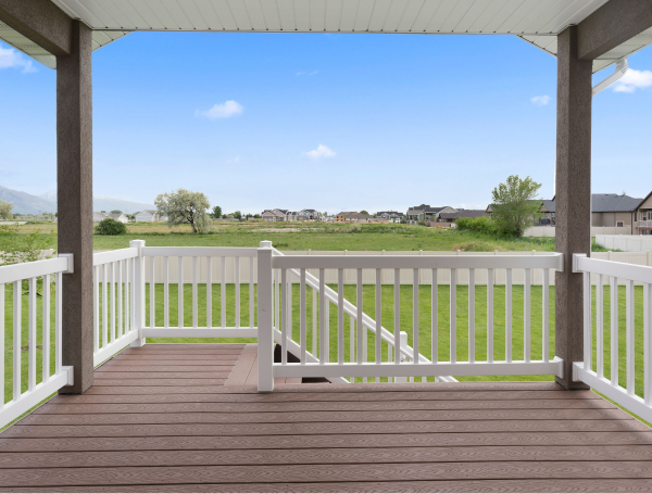 Covered wooden deck with white railings overlooking green field and suburban homes