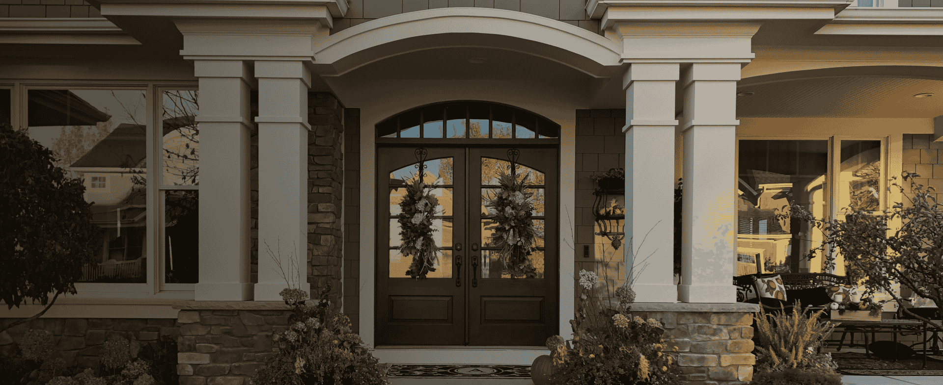 Elegant home entrance with arched doorway, stone columns, and holiday wreaths